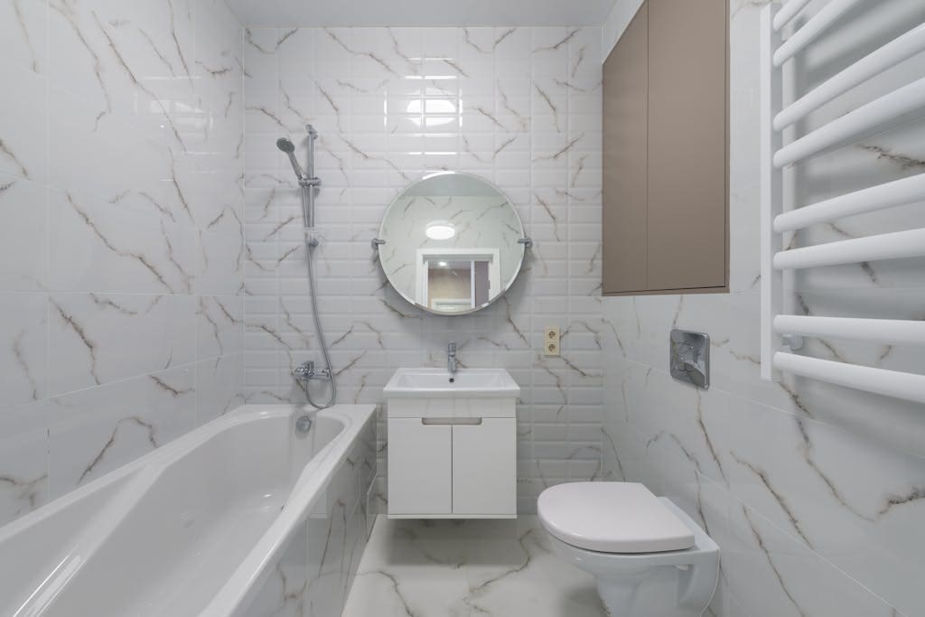 Elegant bathroom with marble tiles, round mirror, and white fixtures.